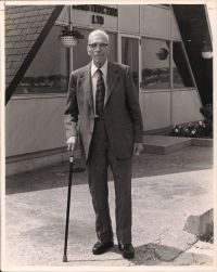 M R Chappell standing while holding cane