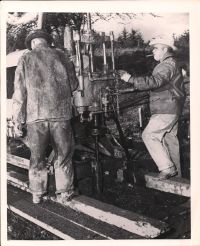 George Greene standing by machine and smoking cigar